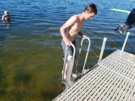 Boy pulling himself out of the water with a dock ladder.