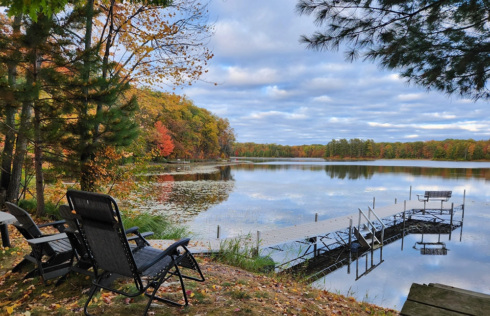 A beautiful lake with a custom portable dock. Two chairs sitting on the shoreline. Fall weather.