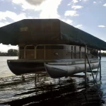 pontoon boat covered with a black canopy stored on a boat lift